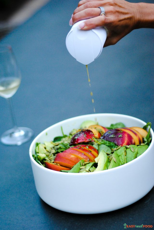 Pouring a homemade dressing over a peach and avocado salad