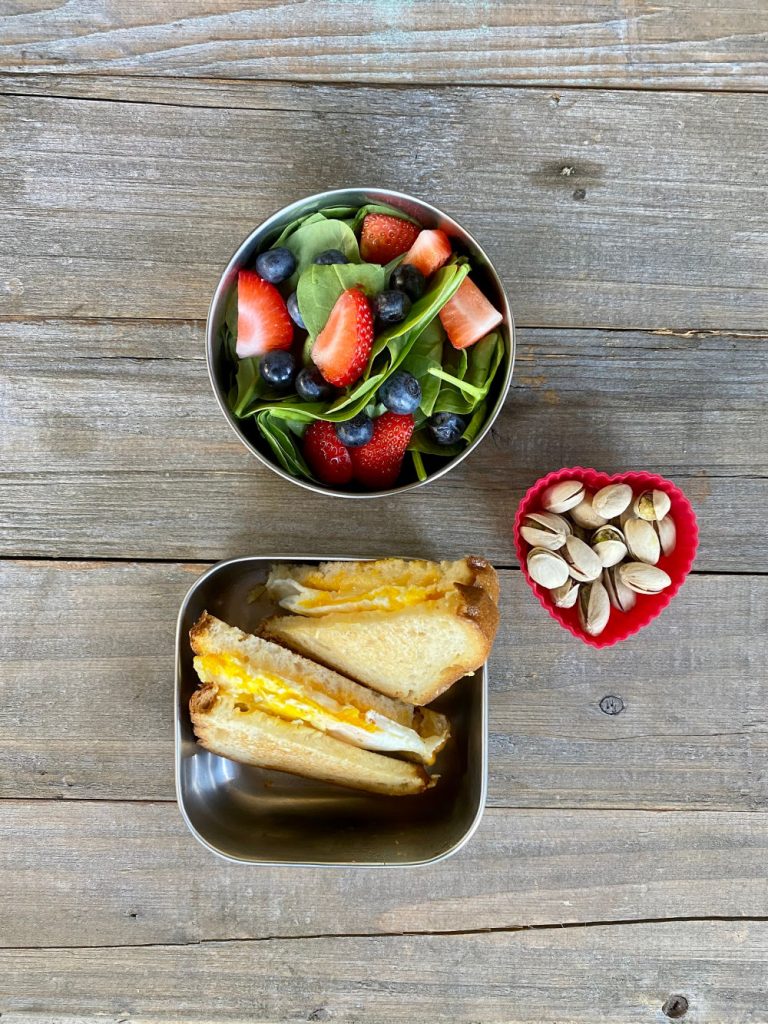 egg and cheese sandwich on gluten free bread, berrie salad on spinach, pistachios