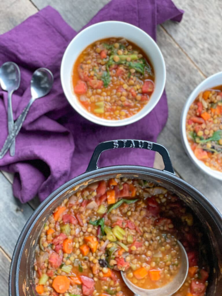 Two bowls of vegetarian lentil soup and a Staub pot with soup in it